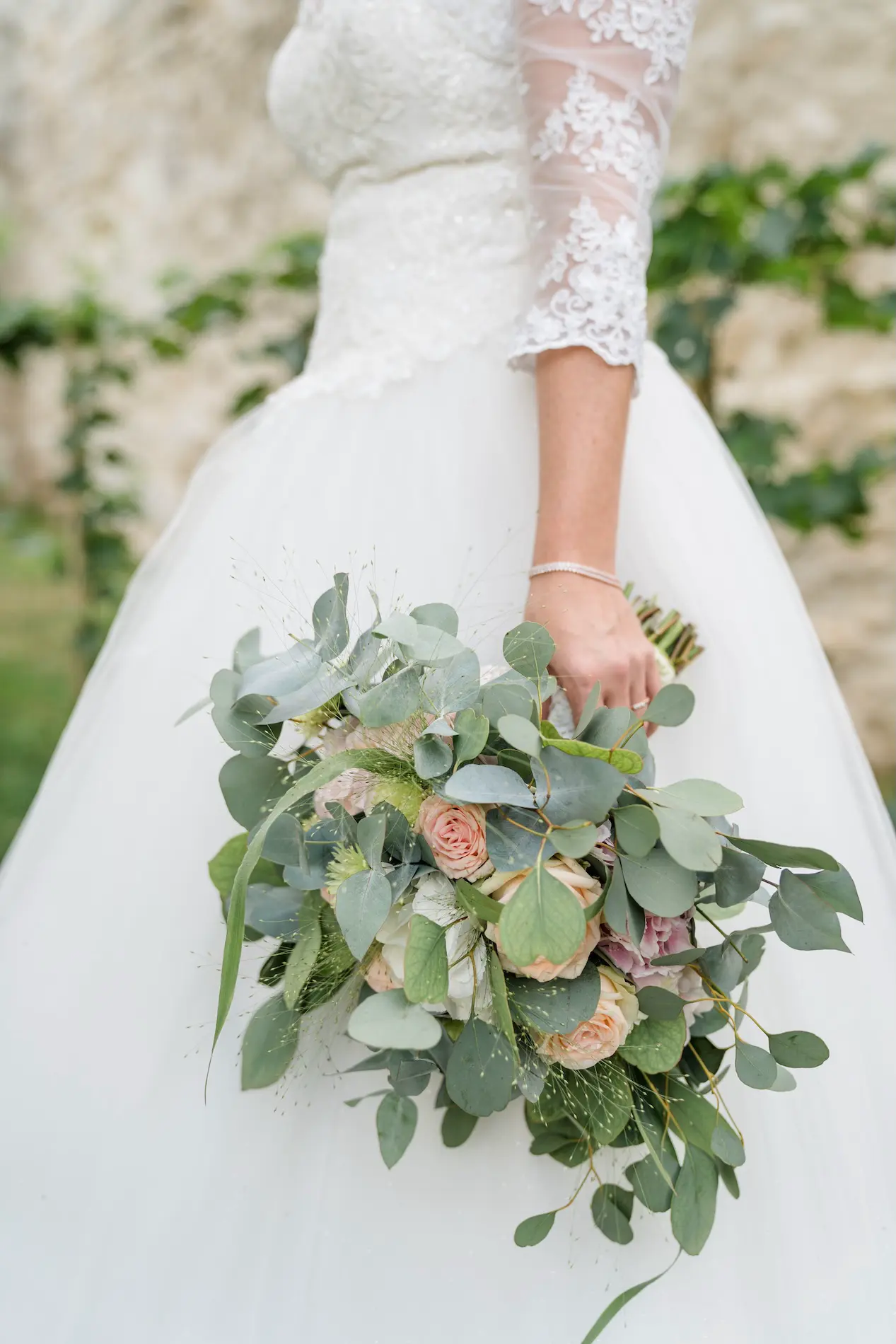 Hochzeitsstraußes mit Eukalyptus, Rosen und grünen Akzenten, gehalten von einer Braut in einem Spitzenkleid.